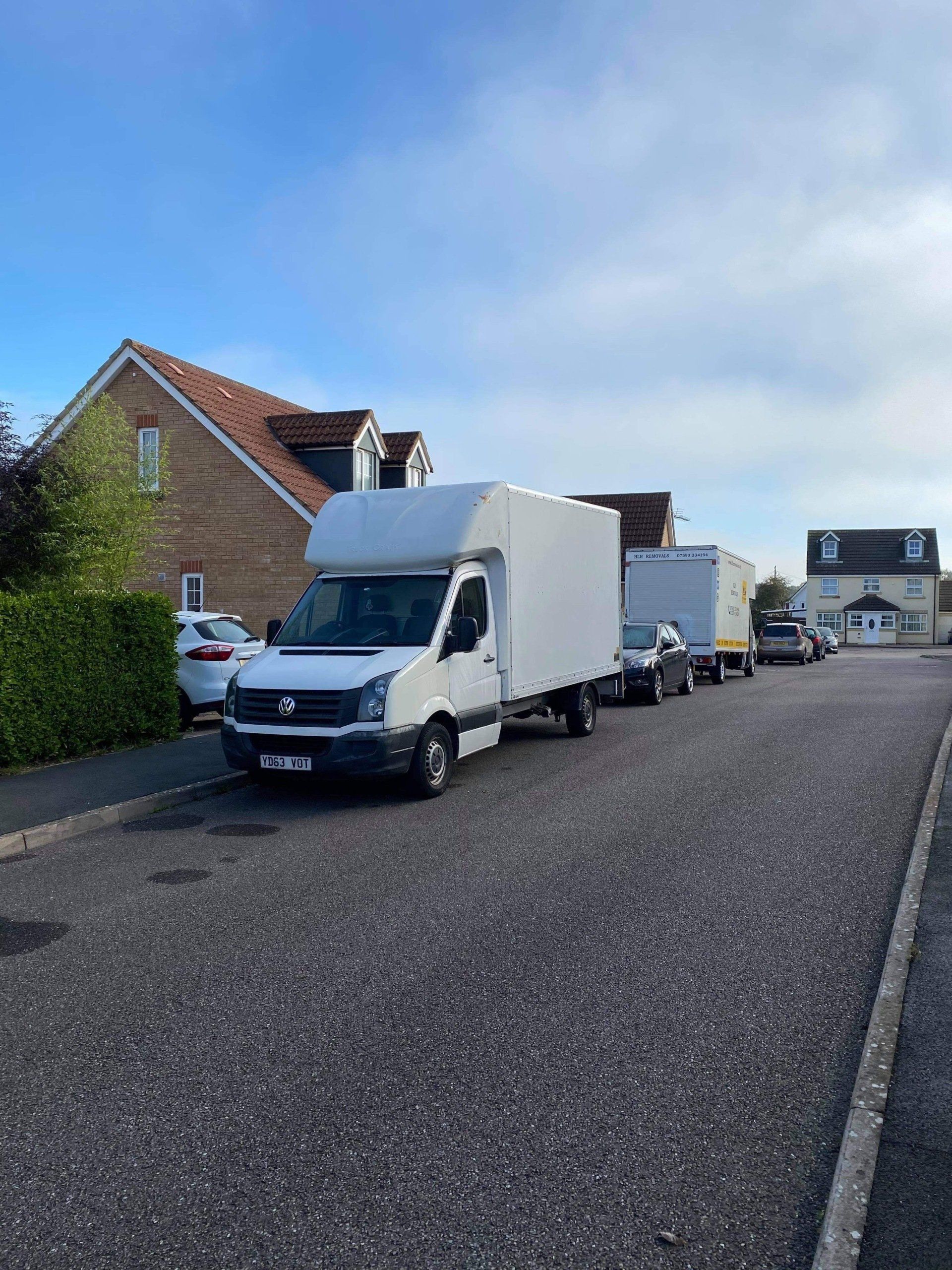 White moving truck with two connected trailers parked on a residential street.