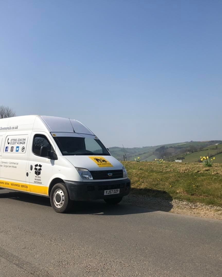White van parked on road; sunny day in countryside setting.