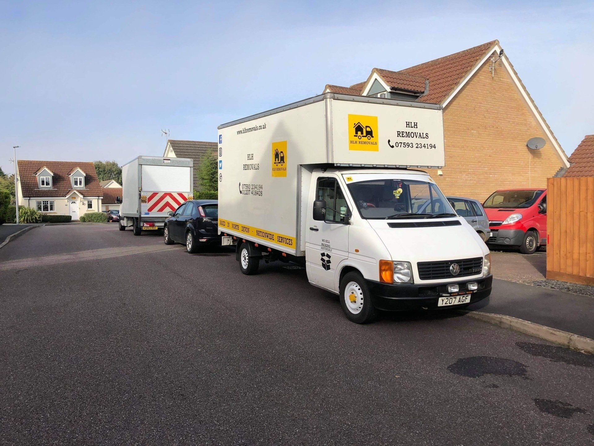 A white moving van and other vehicles parked on a residential street in front of houses.