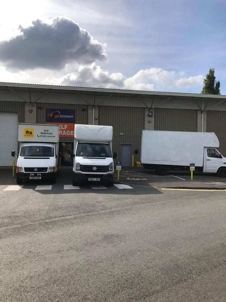 Three white delivery vans parked in front of a storage facility under a cloudy sky.