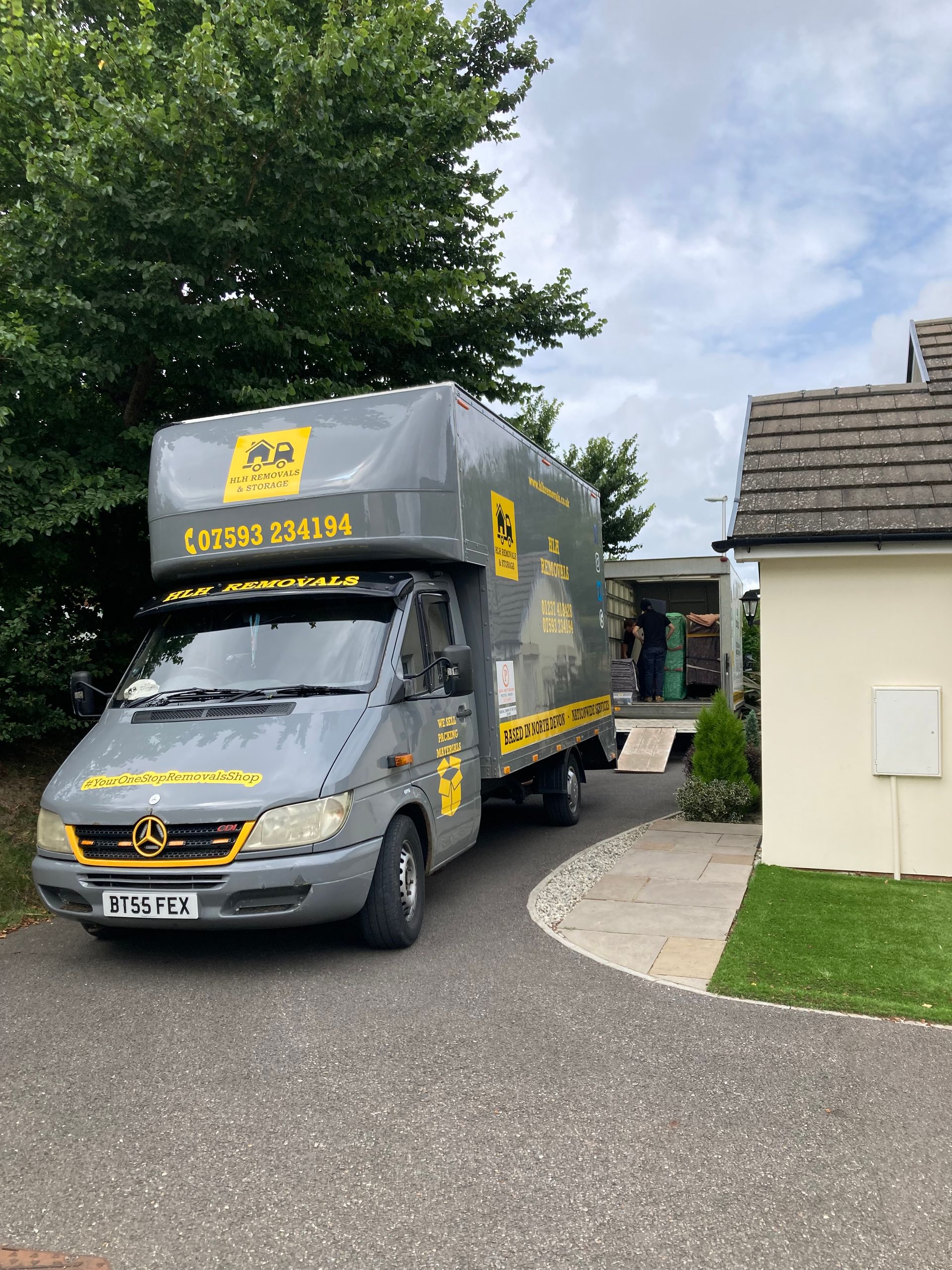 Grey moving truck parked in a driveway, next to a house.