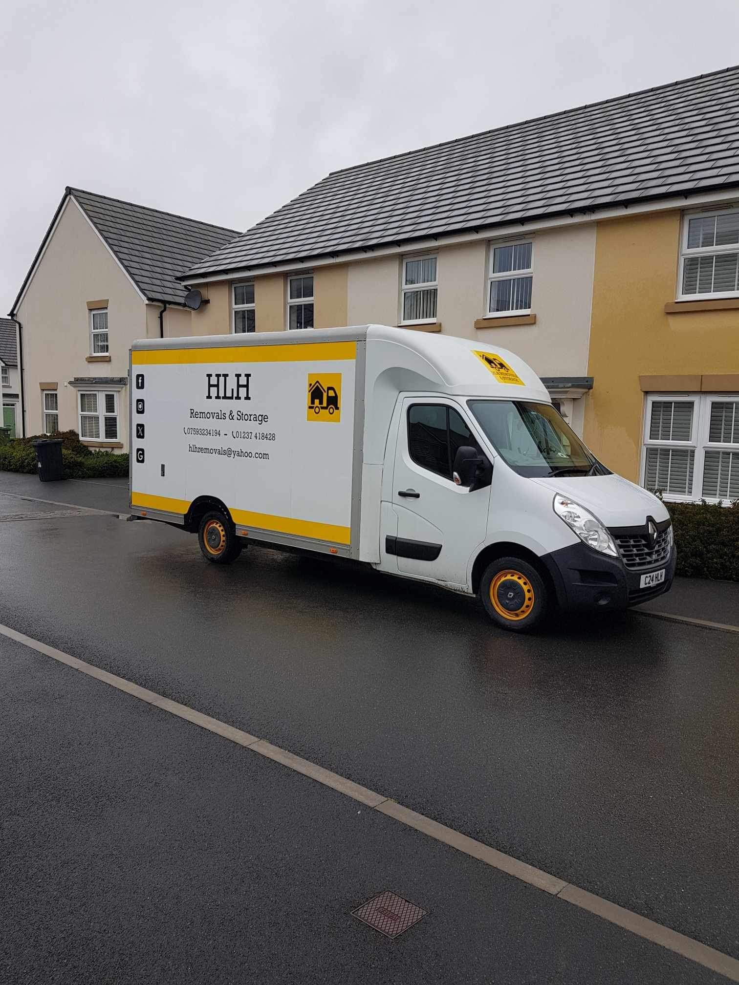 White HLH moving van parked on a street in front of houses on a cloudy day.