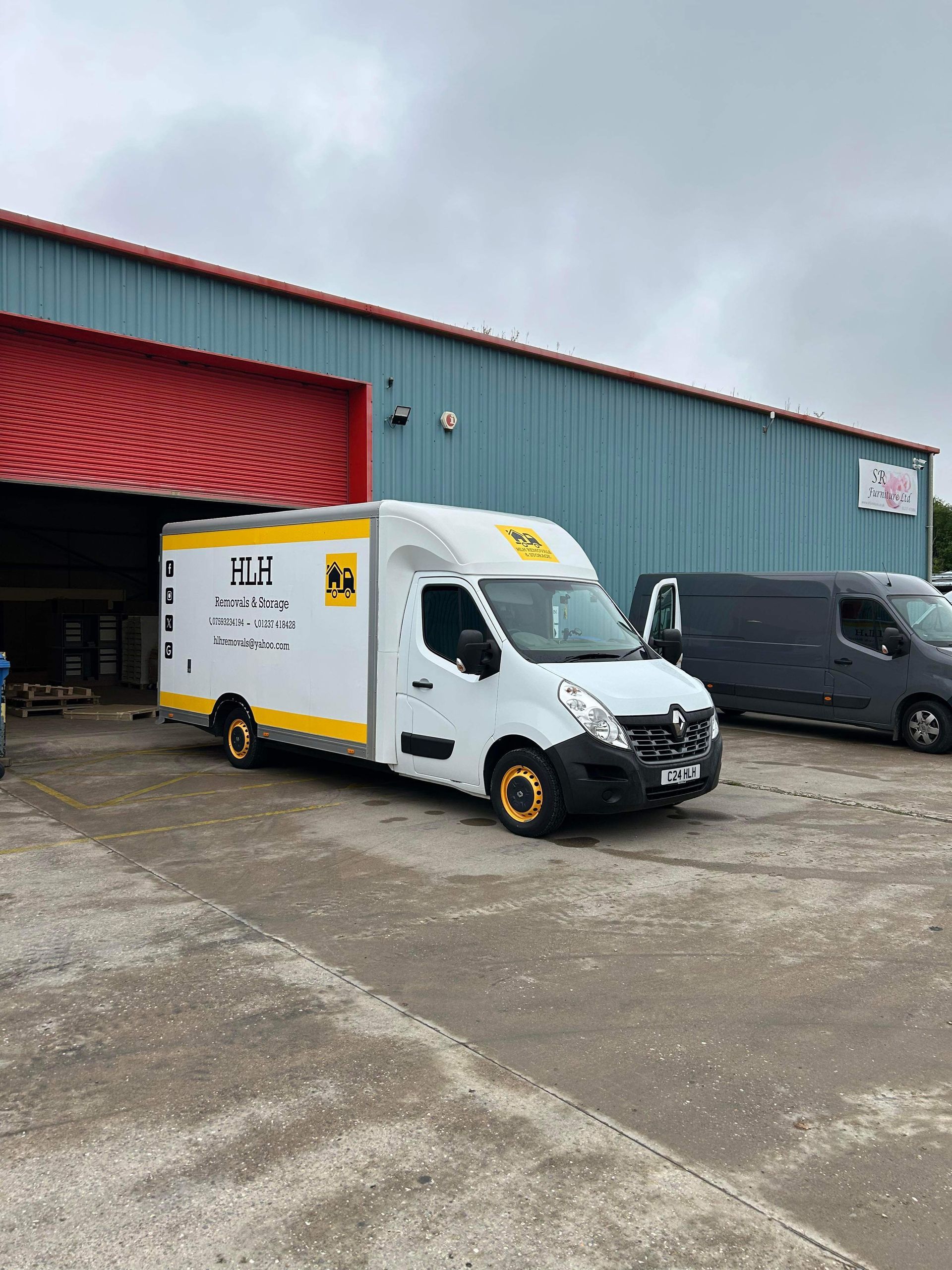 White delivery van with yellow accents parked outside a warehouse with red roof.