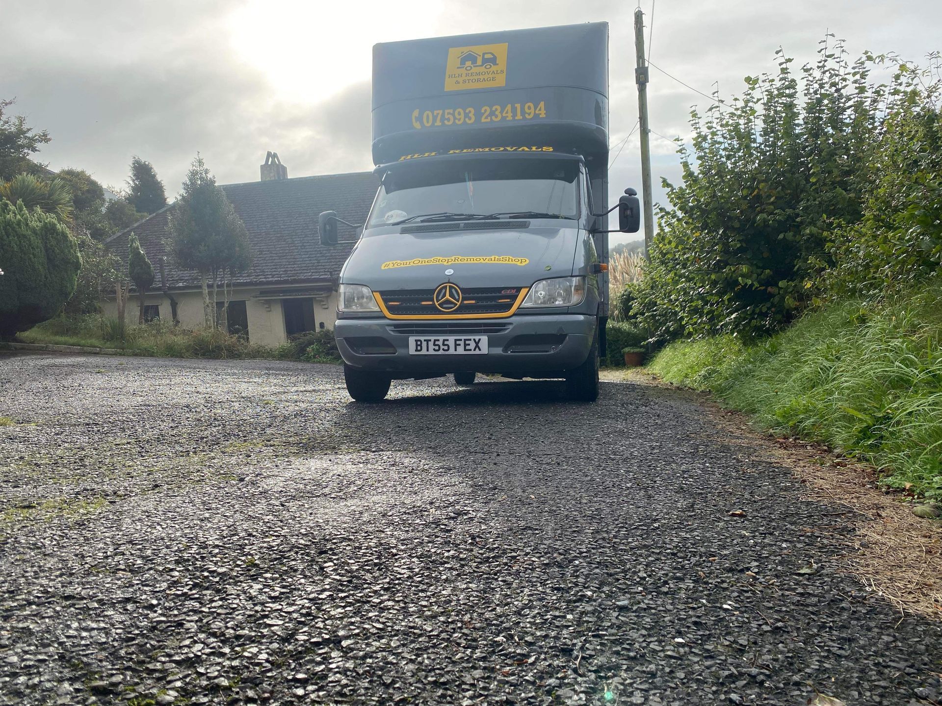 Moving van parked on gravel road in front of a house.