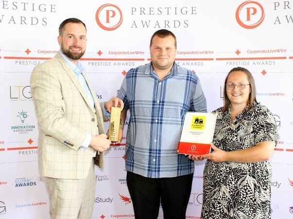 Three people holding awards at a Prestige Awards event; two are smiling.