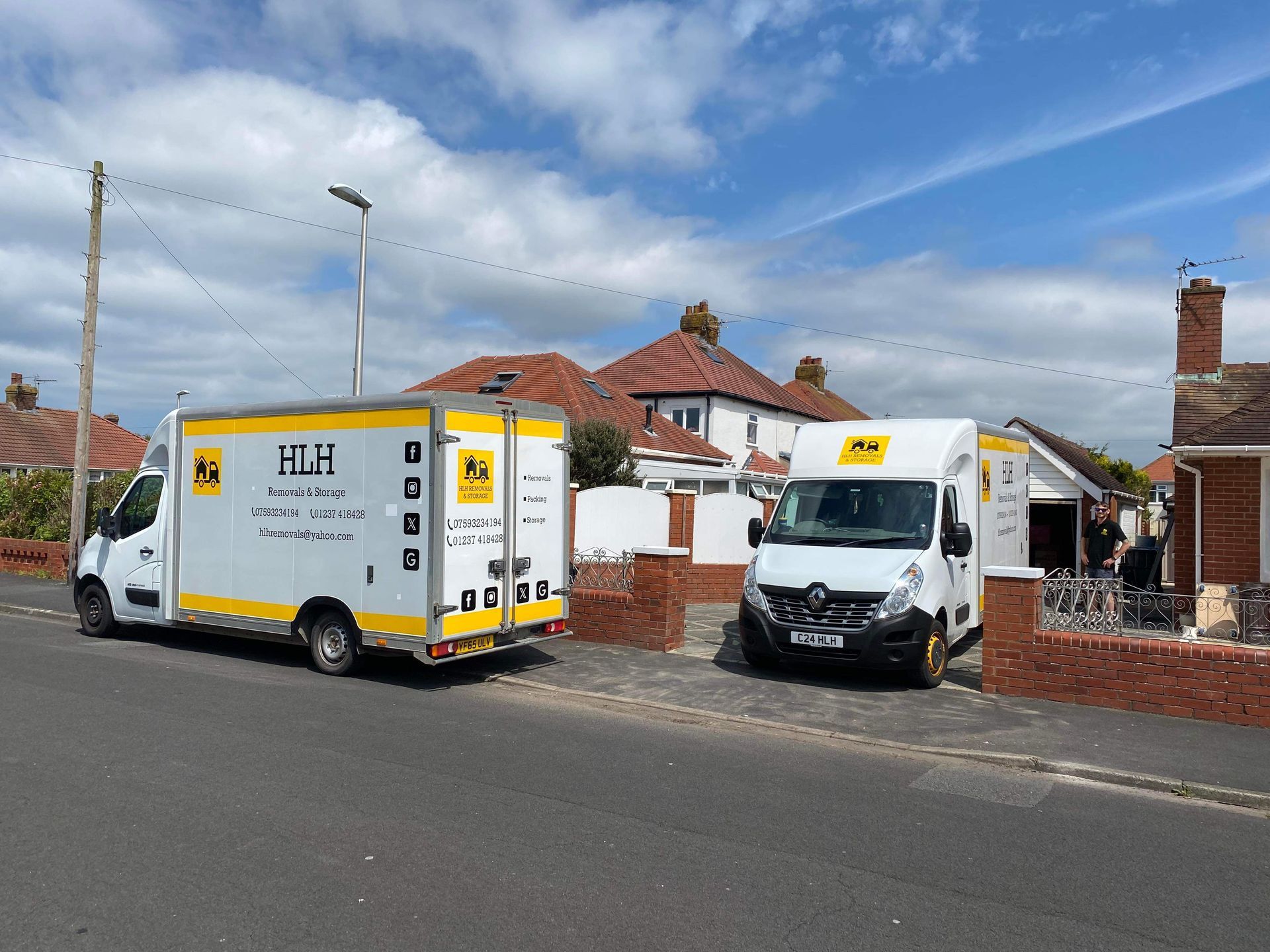 Two white and yellow moving vans parked on a street in front of houses on a sunny day.