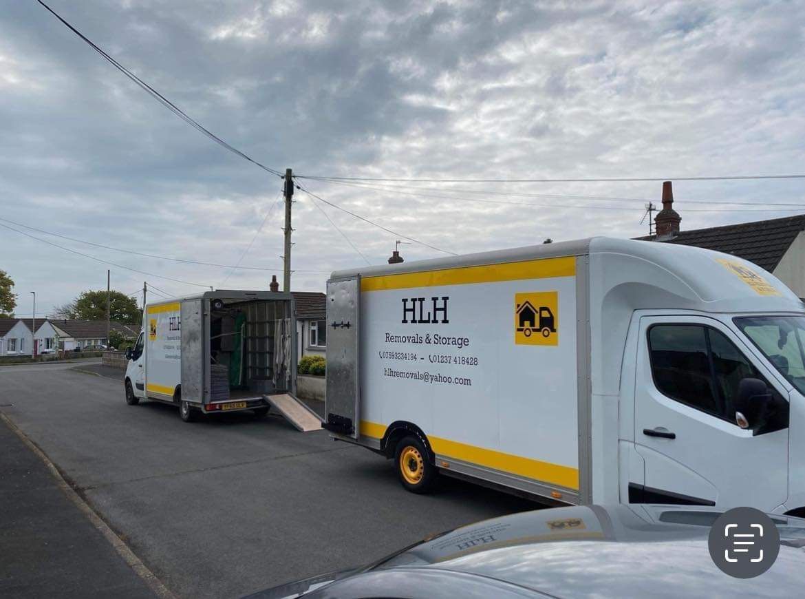 Two white HLH moving vans on a residential street with open rear doors, ready for loading.
