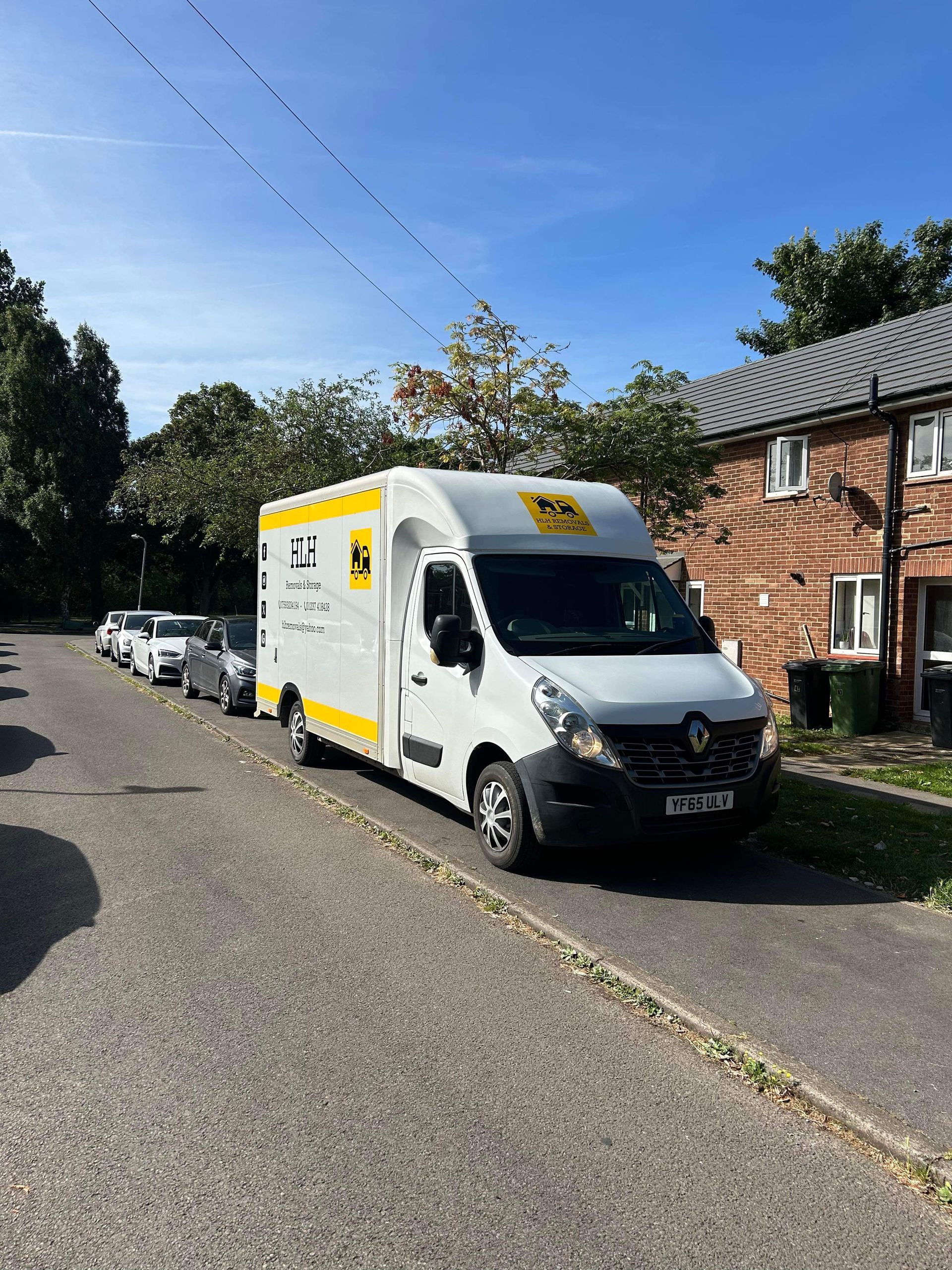 White Royal Mail van parked on a residential street; several cars parked behind it under a blue sky.