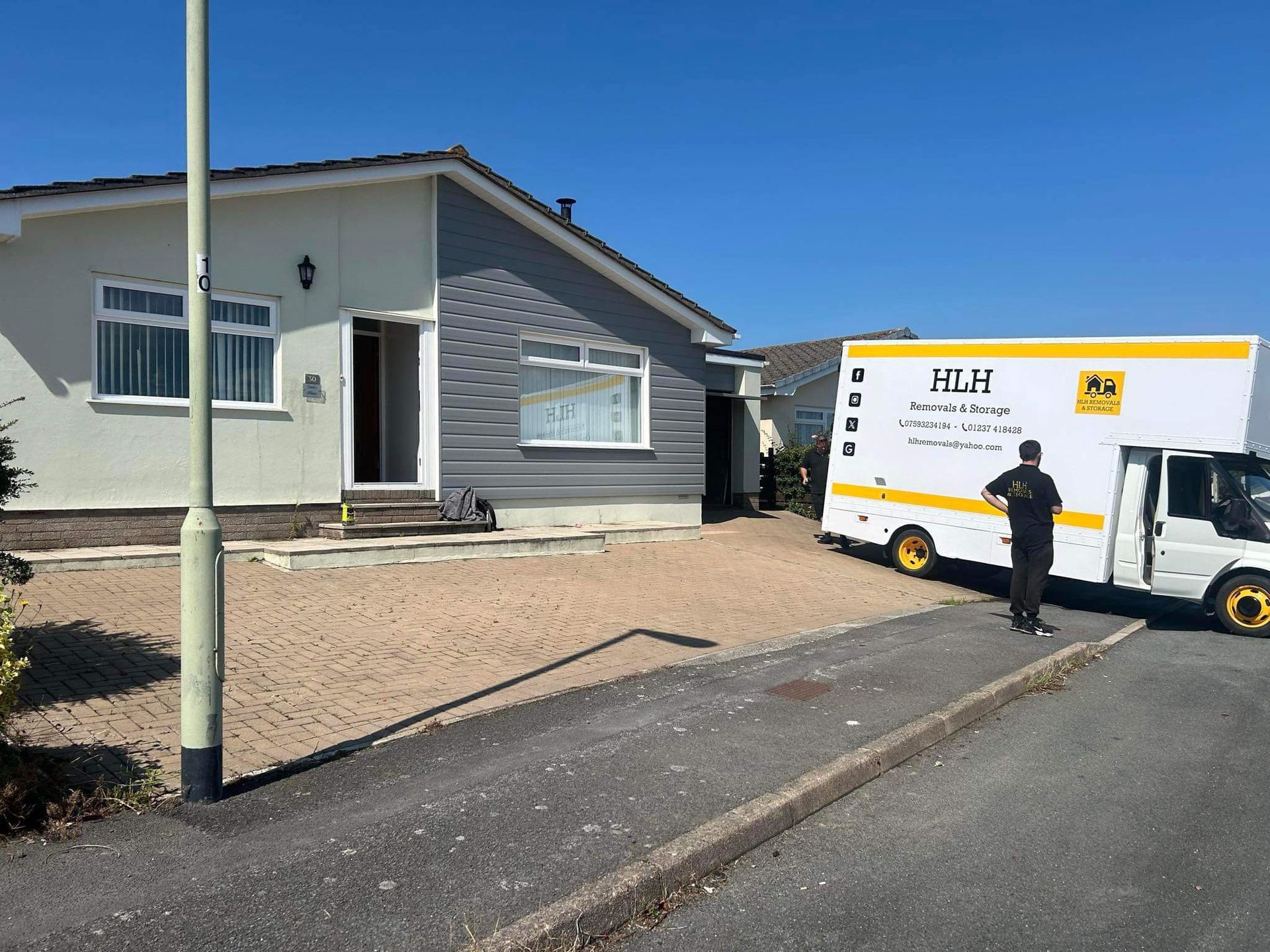 A moving truck parked in front of a house. A person stands near the truck on a sunny day.