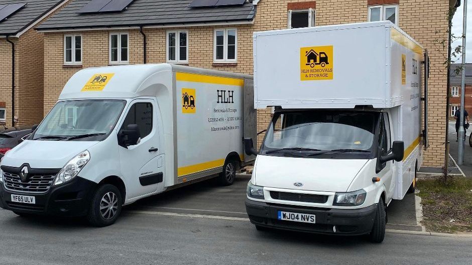 Two white moving vans parked outside houses. The vans have yellow logos.