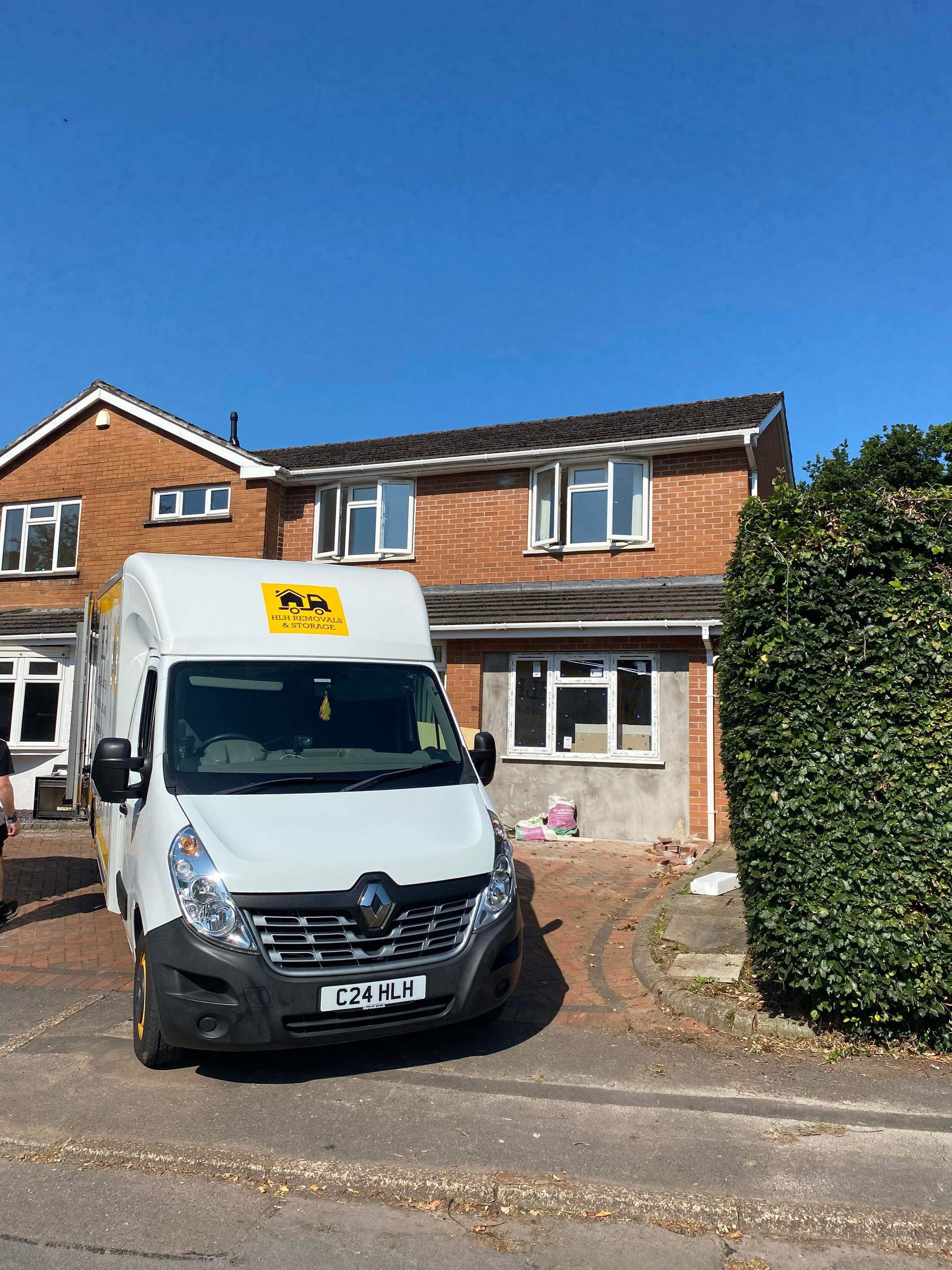 White van parked in front of a two-story brick house; clear blue sky above.