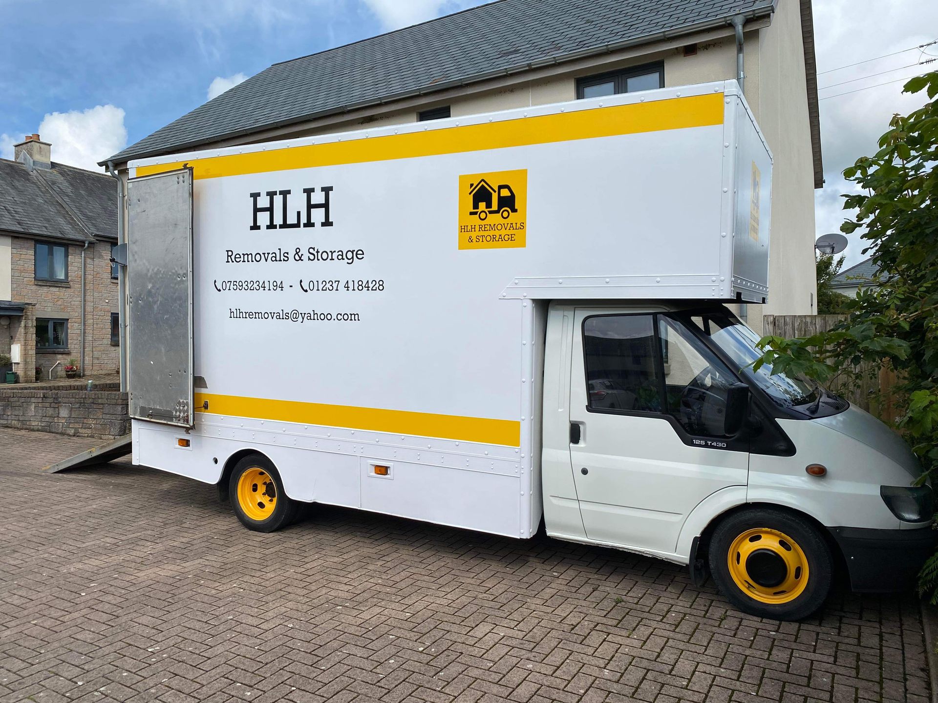 White HLH moving truck parked near a house, with yellow accents and logo.