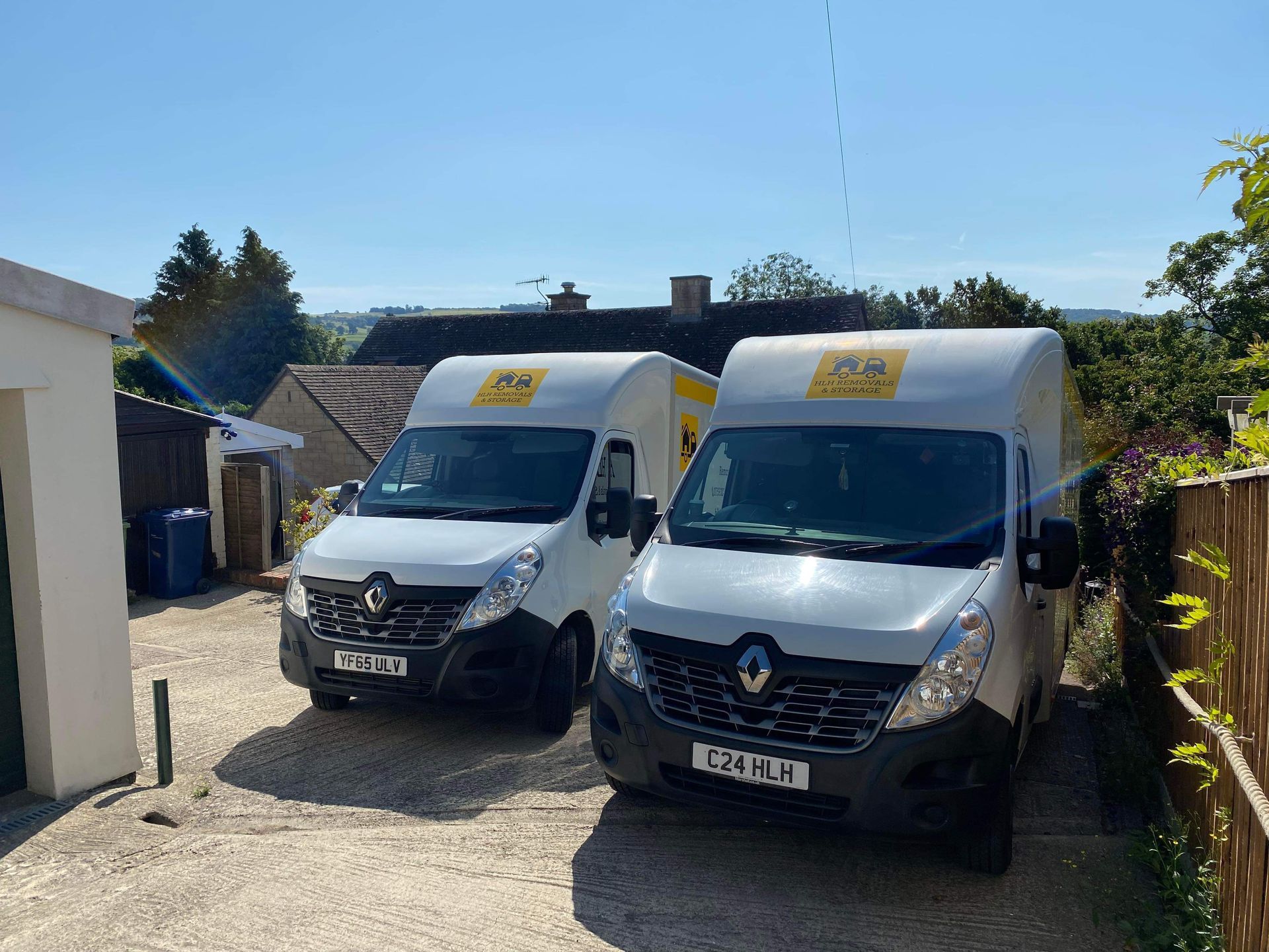 Two white vans with yellow logos parked outside a building on a sunny day.