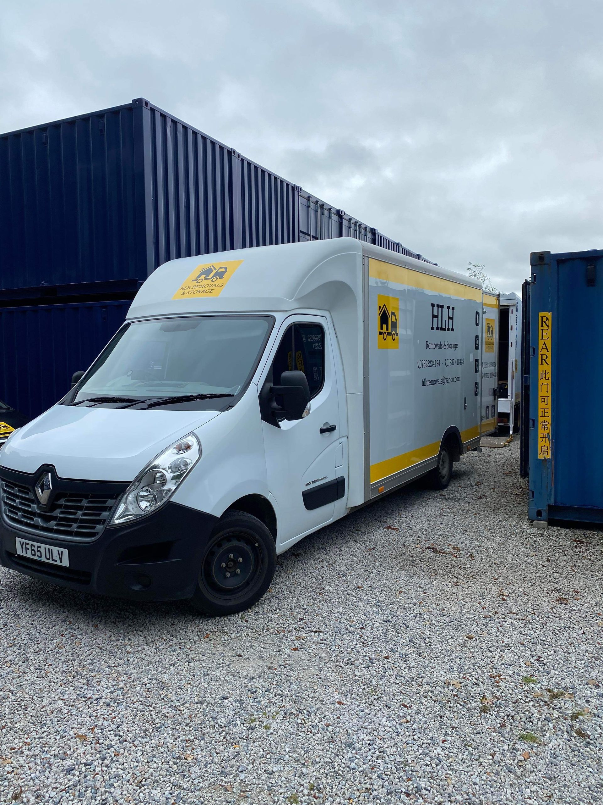 White Renault Master van with yellow accents parked on gravel, near blue containers.