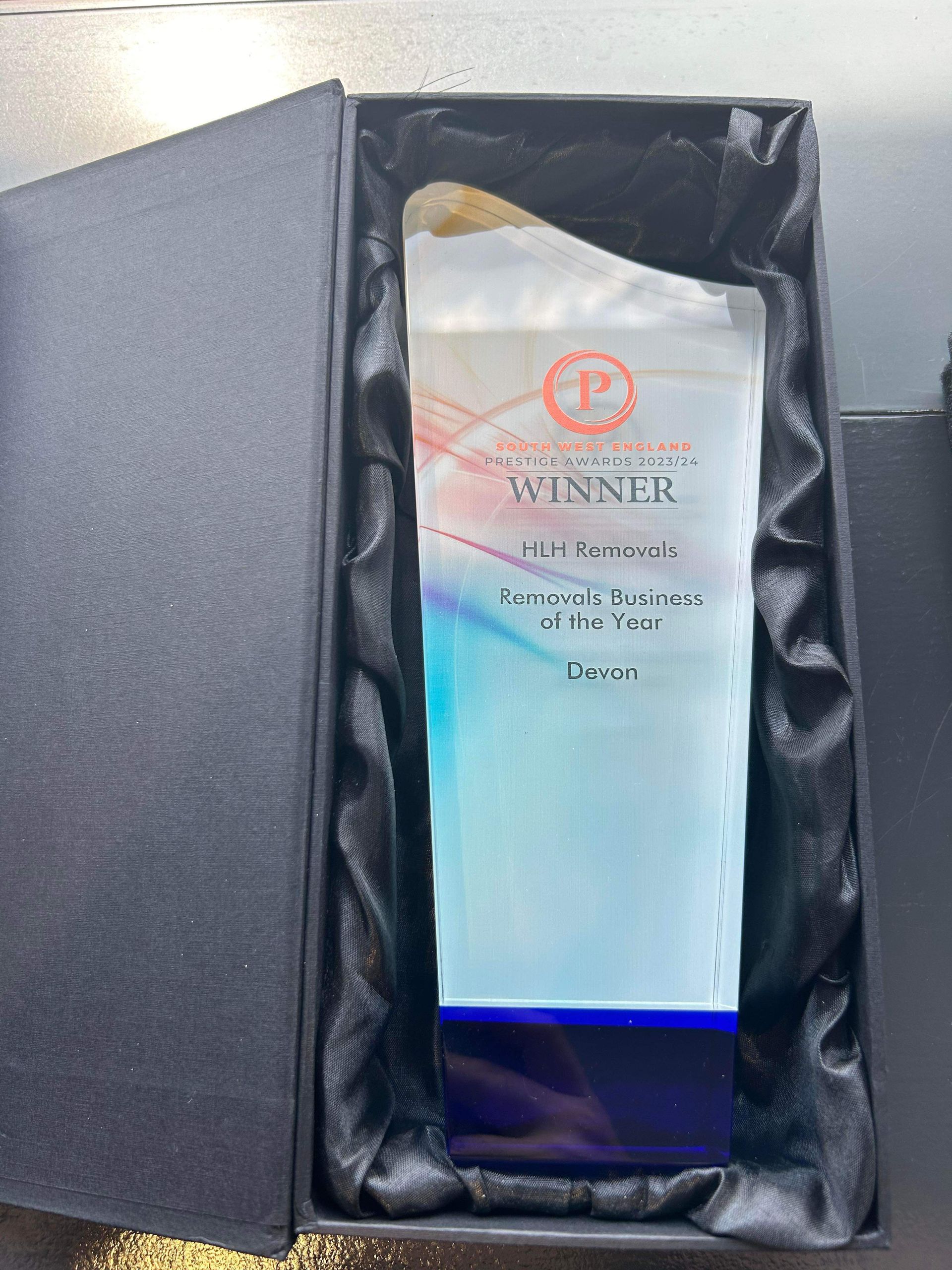 Award trophy in a black box; glass with blue, red, and white design; says 