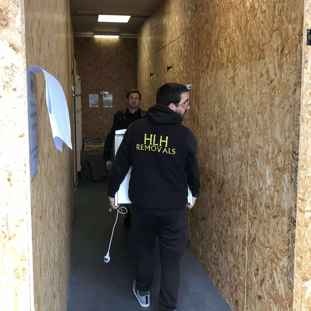 Two movers in a narrow hallway, one carrying a box, wearing a 