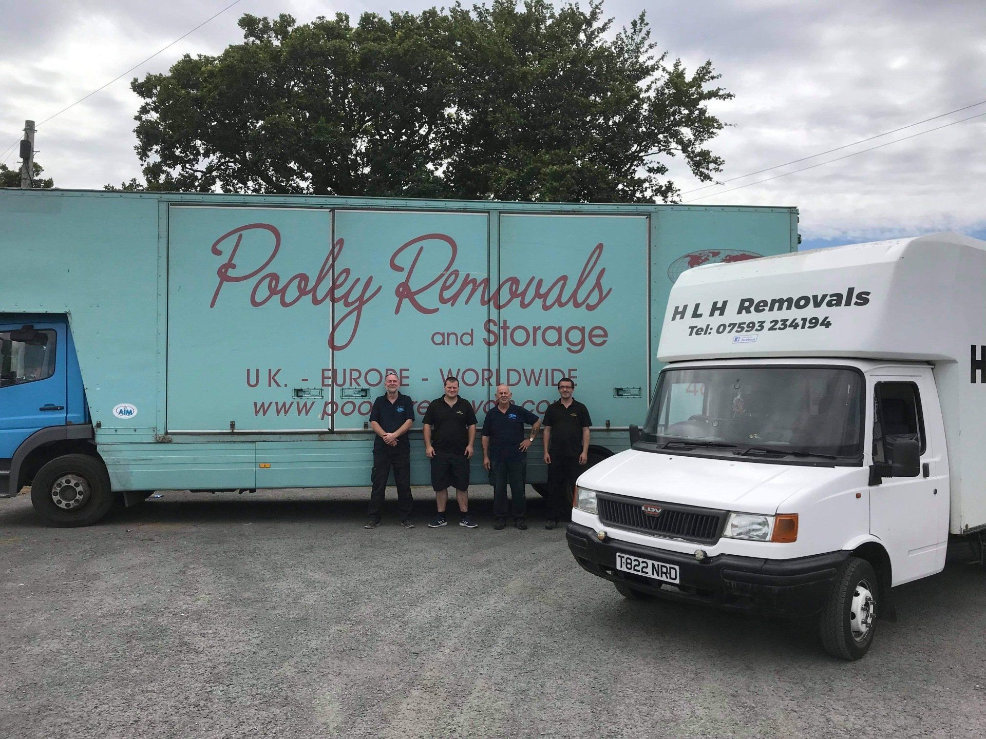Four men standing in front of two moving trucks: a blue one with 