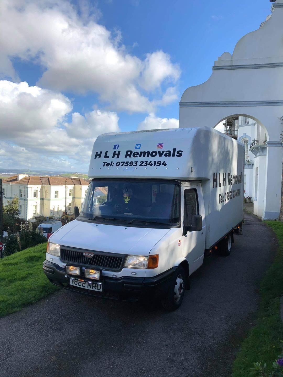 White HLR Removals van parked on a hill in front of a white building on a sunny day.
