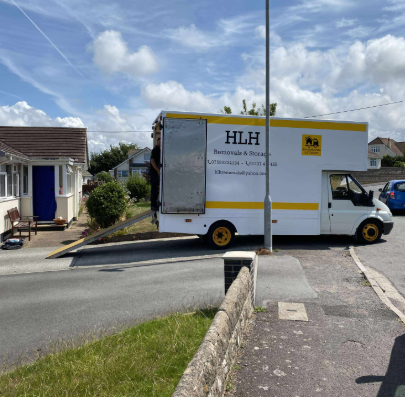 White HLH removals truck parked on a residential street, doorway open, sunny day.