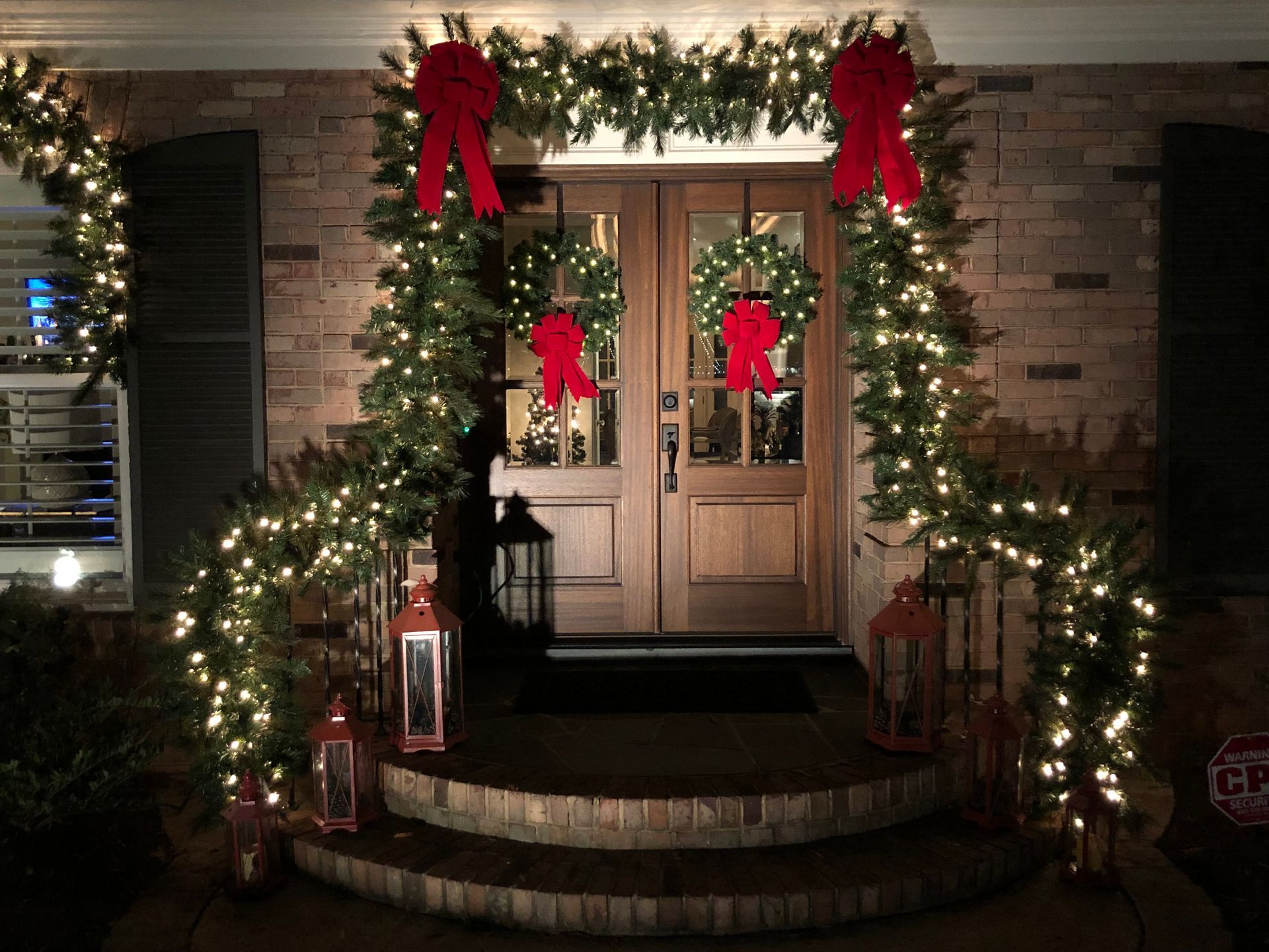 Christmas decorated front door with wreaths, garland, red bows, and lanterns.