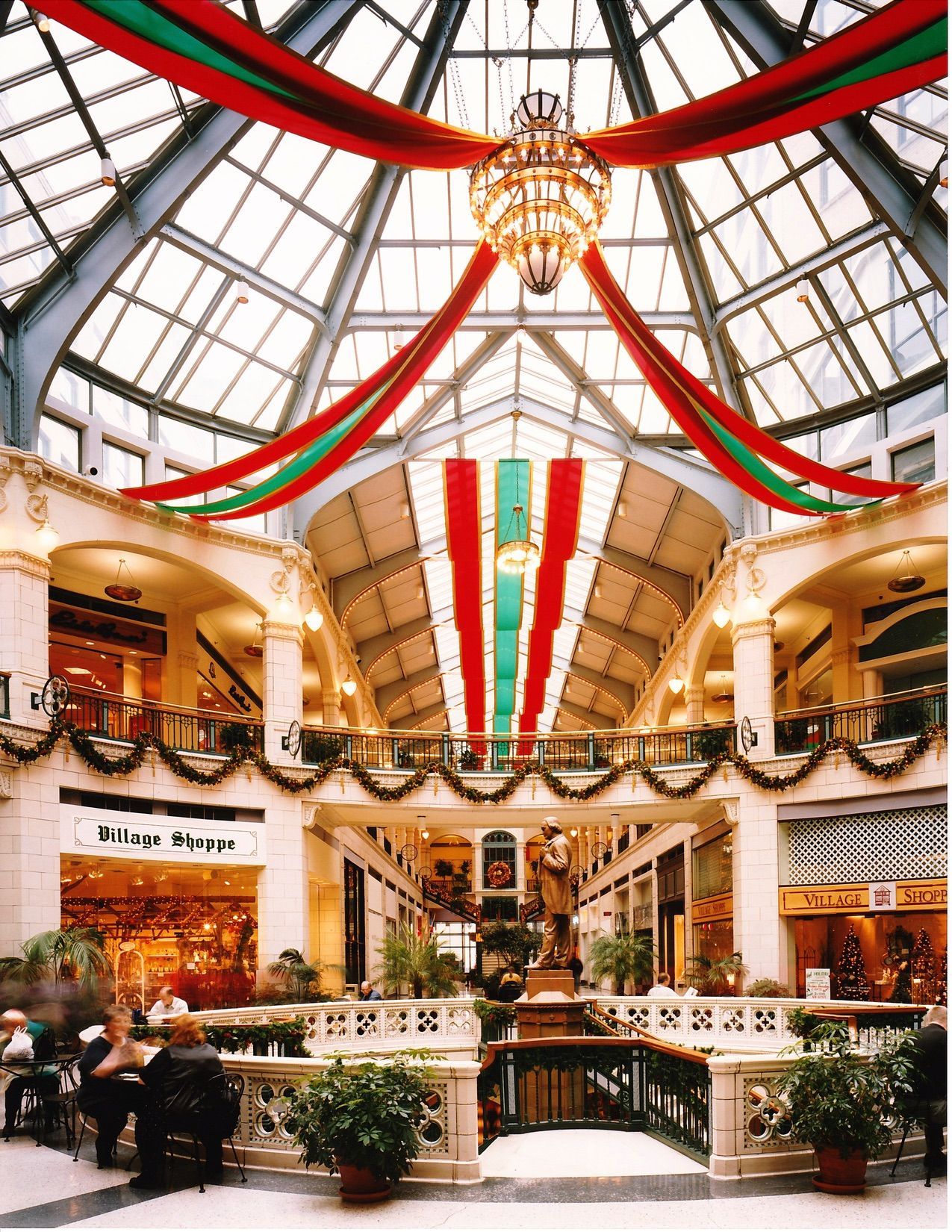 An ornate indoor shopping mall decorated with festive red and green ribbons.