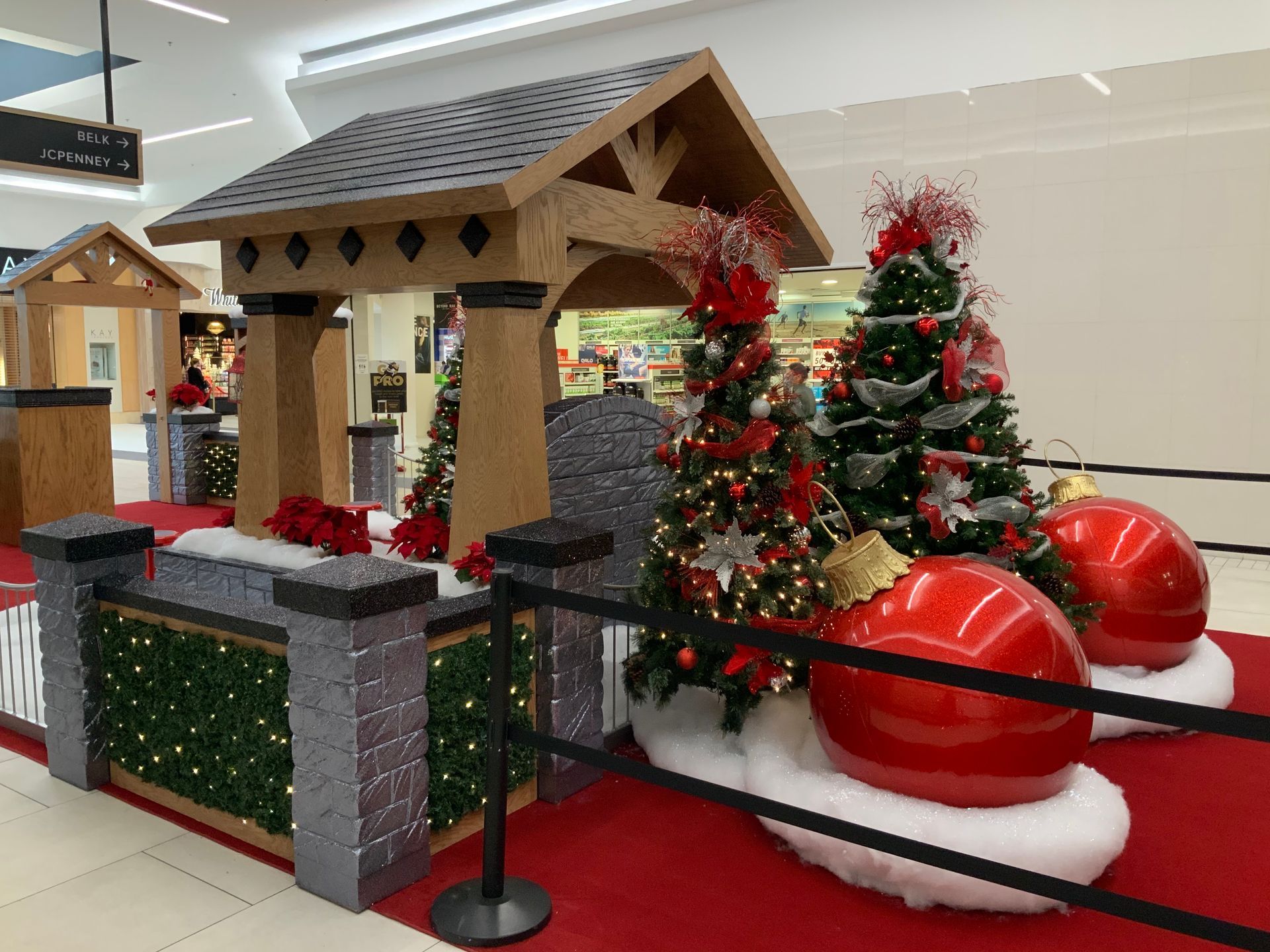 Christmas display in a mall with trees, large red ornaments, and a wooden gazebo.