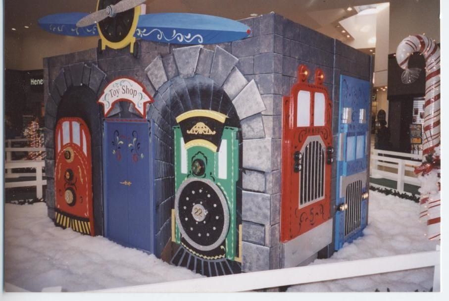 A child's playhouse in the shape of a train with colorful doors, faux snow, and an airplane topper.