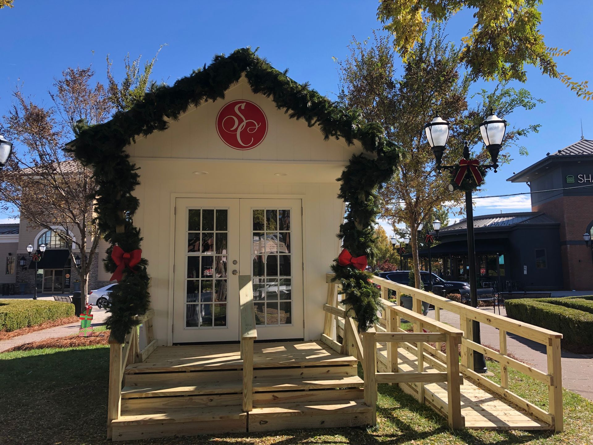 Small white building with ramp, decorated with garland, red bows, and logo.