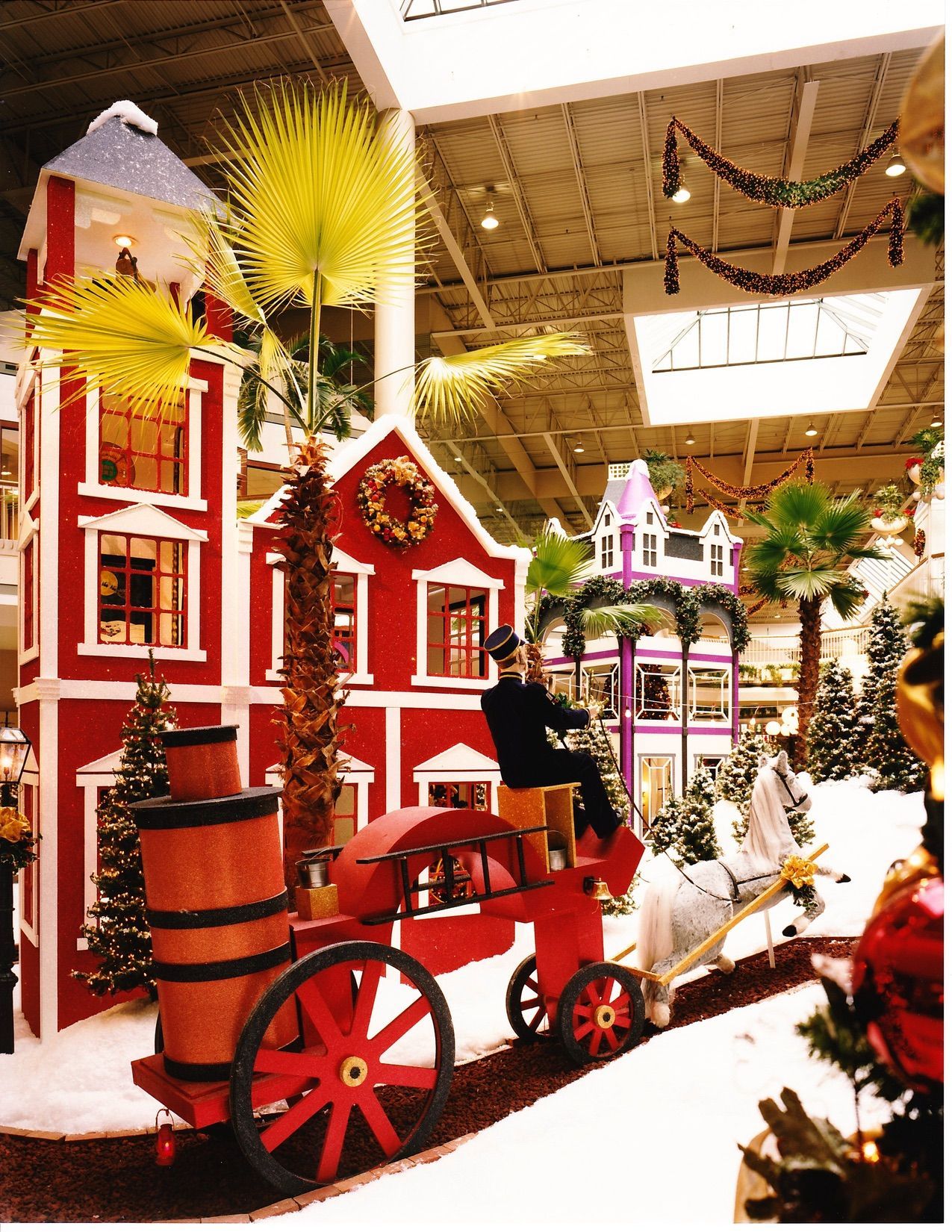 Holiday display in a mall with red buildings, a horse-drawn carriage, and decorations.