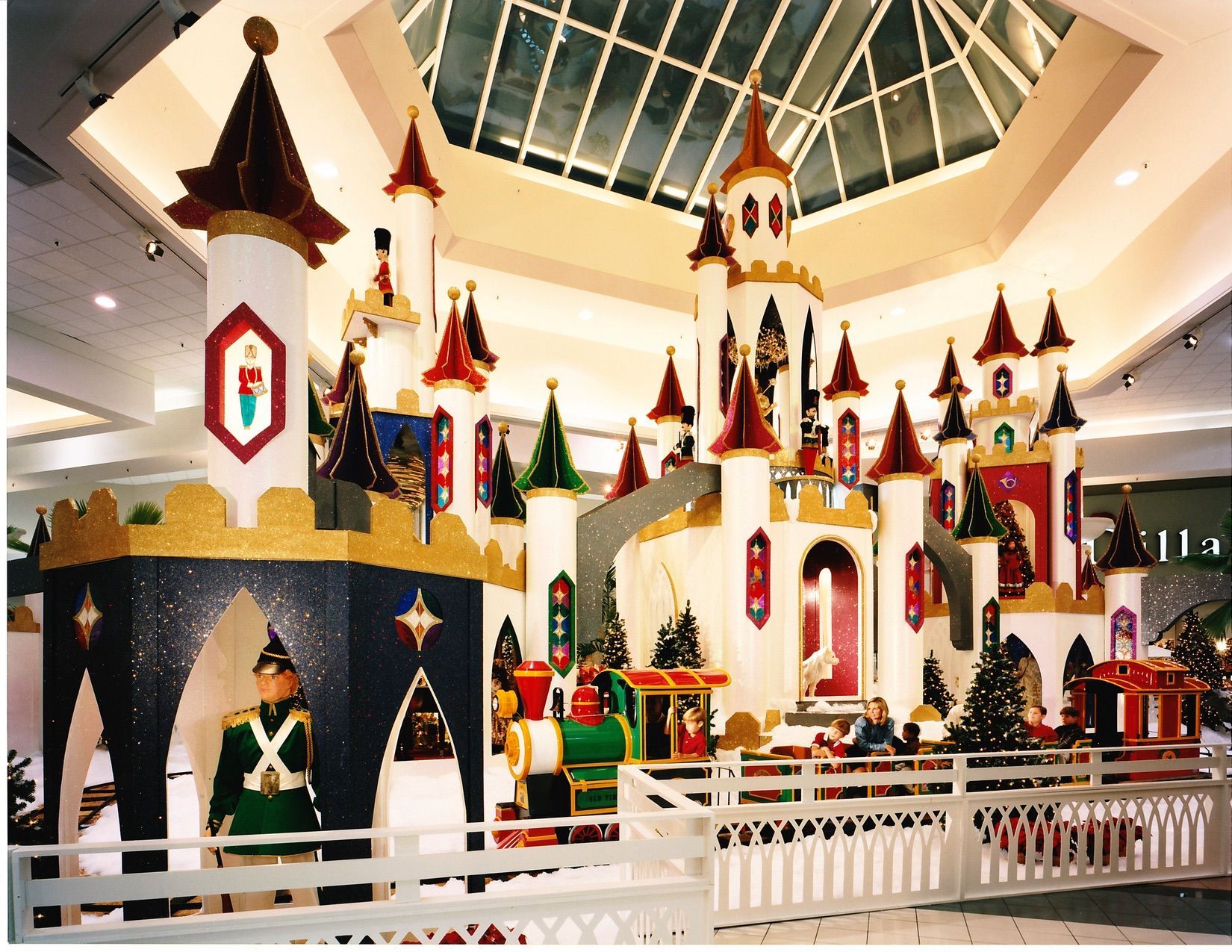 Holiday display: Colorful castle with turrets, train, and toy soldiers in a mall atrium.