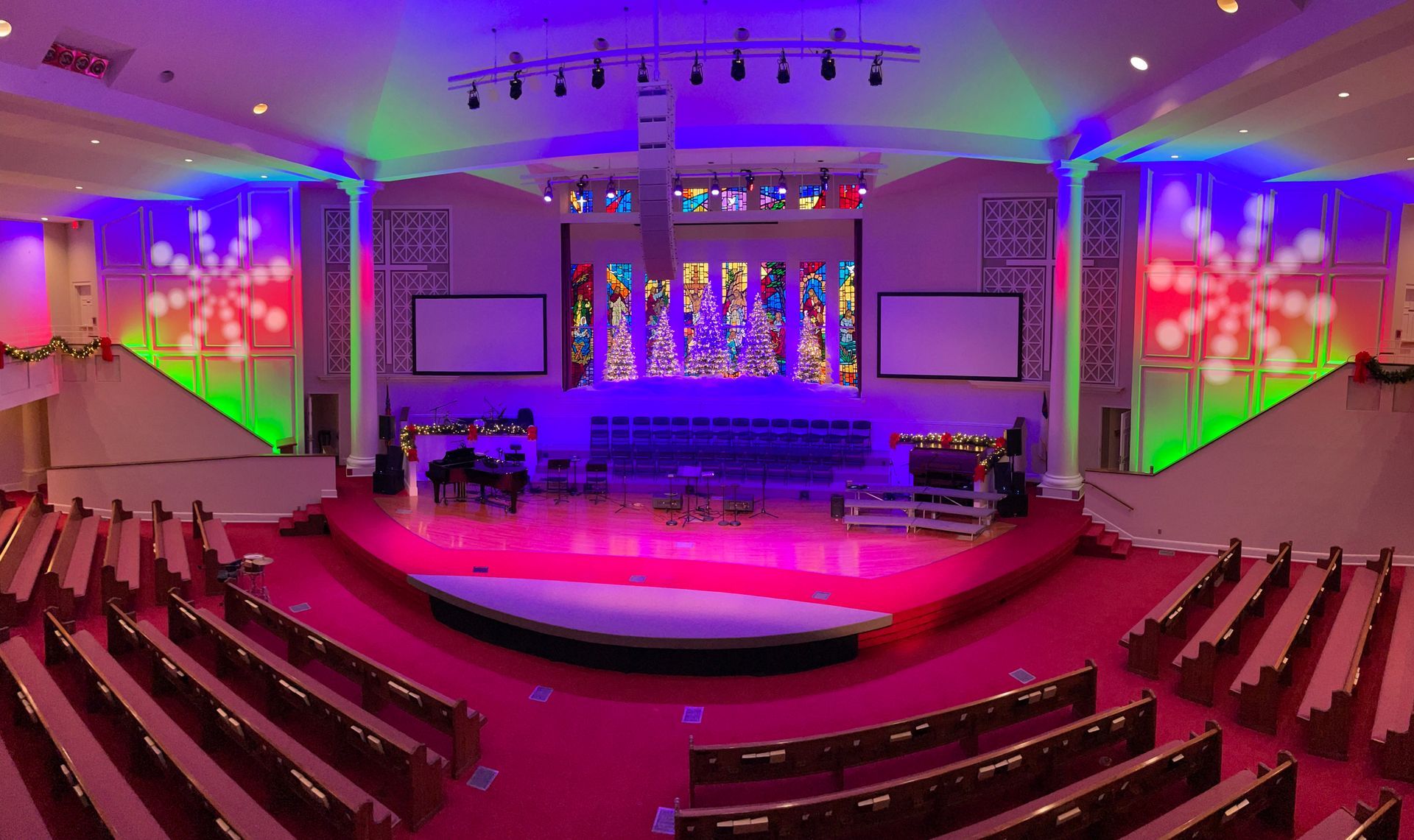 Church sanctuary with red carpet, rows of seats, stage with colorful lights.