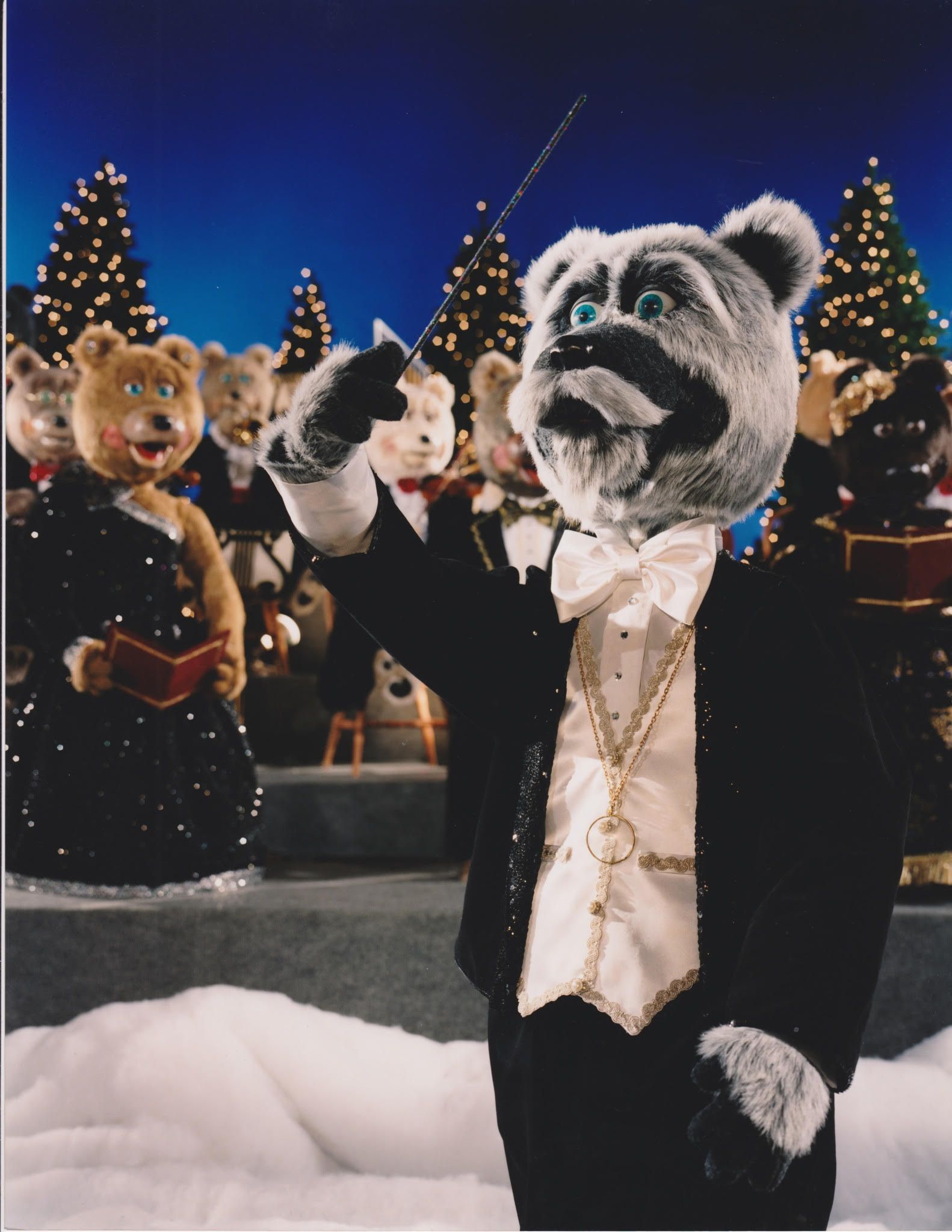 Conductor bear in tuxedo leading a bear orchestra in front of Christmas trees, with a snowy background.