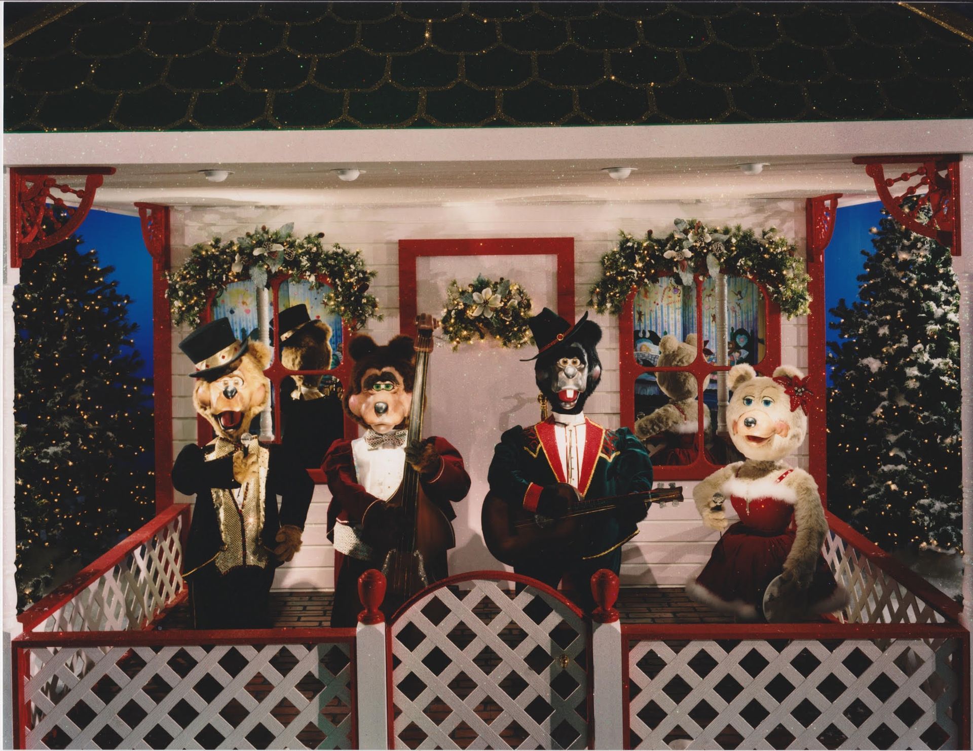 Animated bear figures dressed in formal attire on a stage decorated for Christmas.