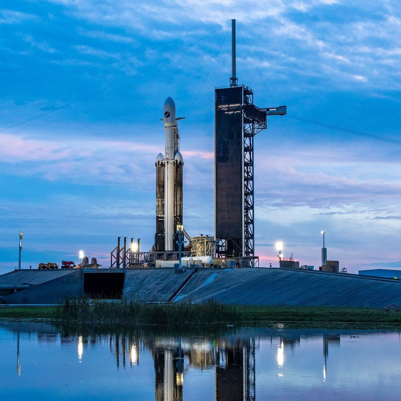 A rocket is sitting on top of a building next to a body of water.