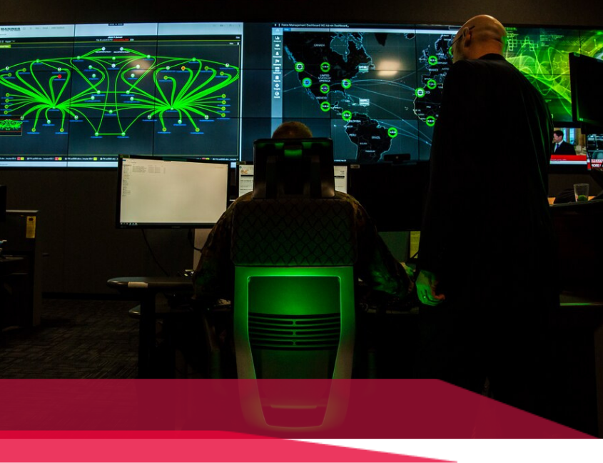 Inside a security operations center, people monitor screens displaying network diagrams. Green glows.