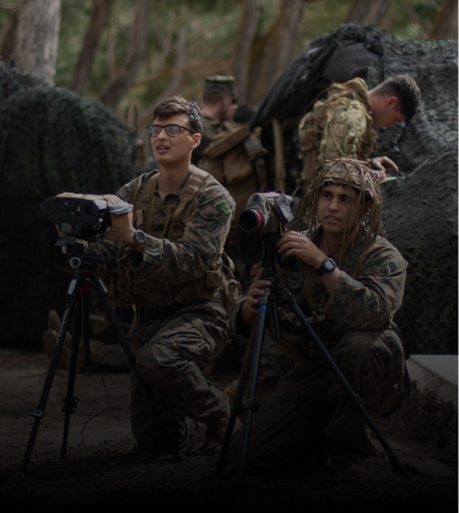 A group of soldiers are kneeling down and looking through binoculars