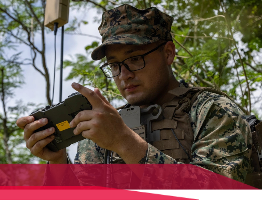 Marine in camouflage operating a handheld device outdoors, likely controlling a drone.