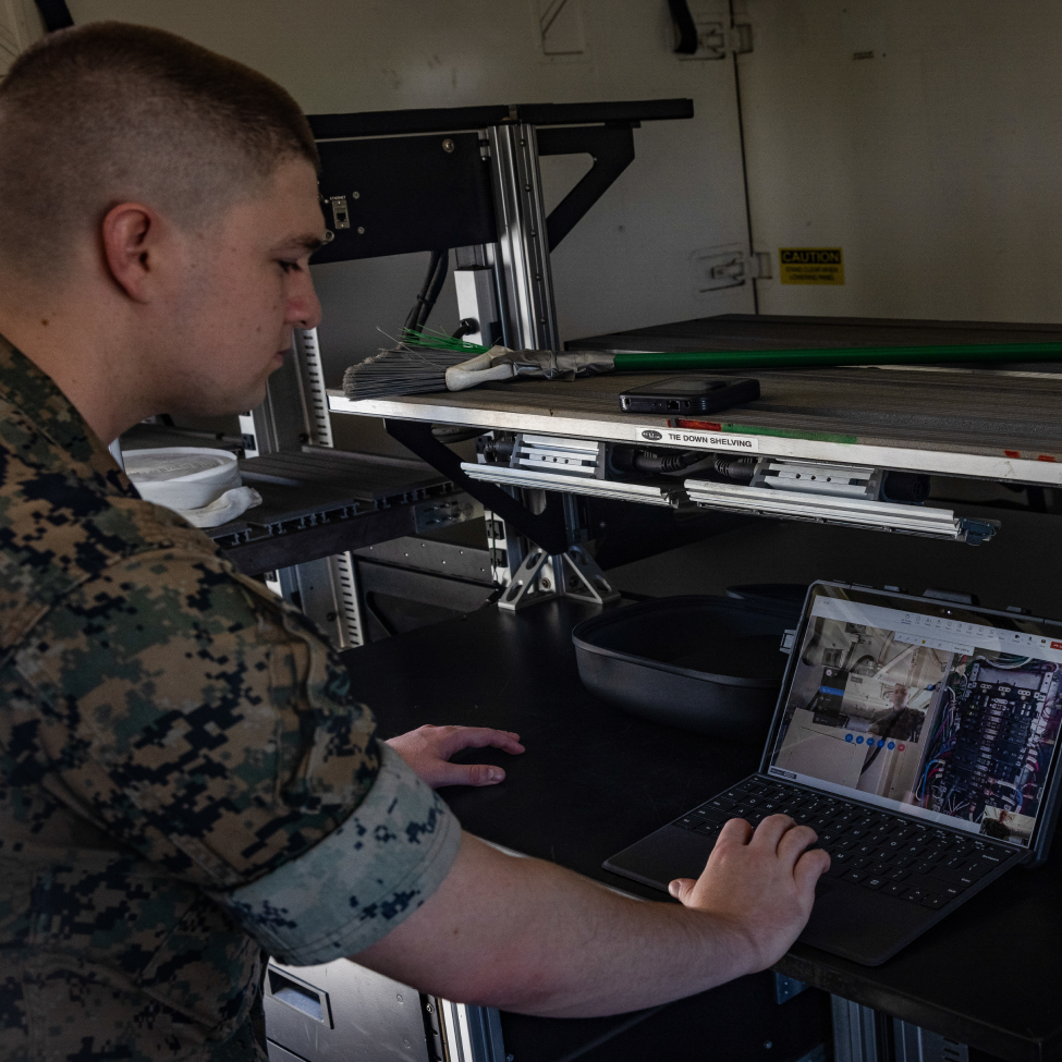 A man in a camo uniform is typing on a laptop