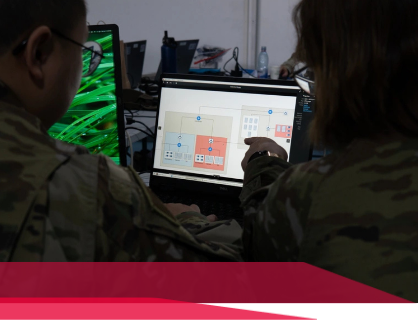 Two people in military uniforms looking at a laptop screen with a map and icons, possibly discussing strategy.