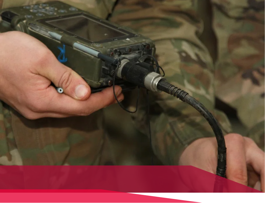 A person in a military uniform is holding a device with a cord attached to it.