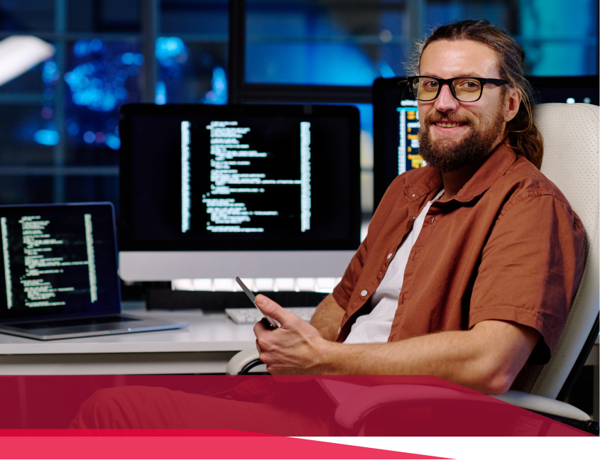 A man is sitting in front of a computer holding a cell phone.