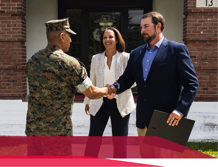 A man in a military uniform shakes hands with a man in a suit