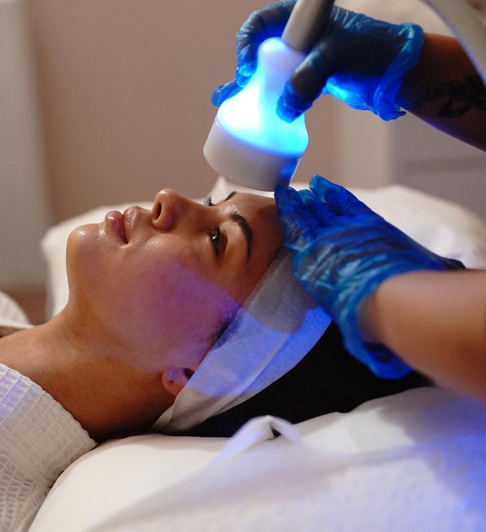 Woman receiving a facial treatment with a blue-light device. Hands in blue gloves perform procedure in a spa.