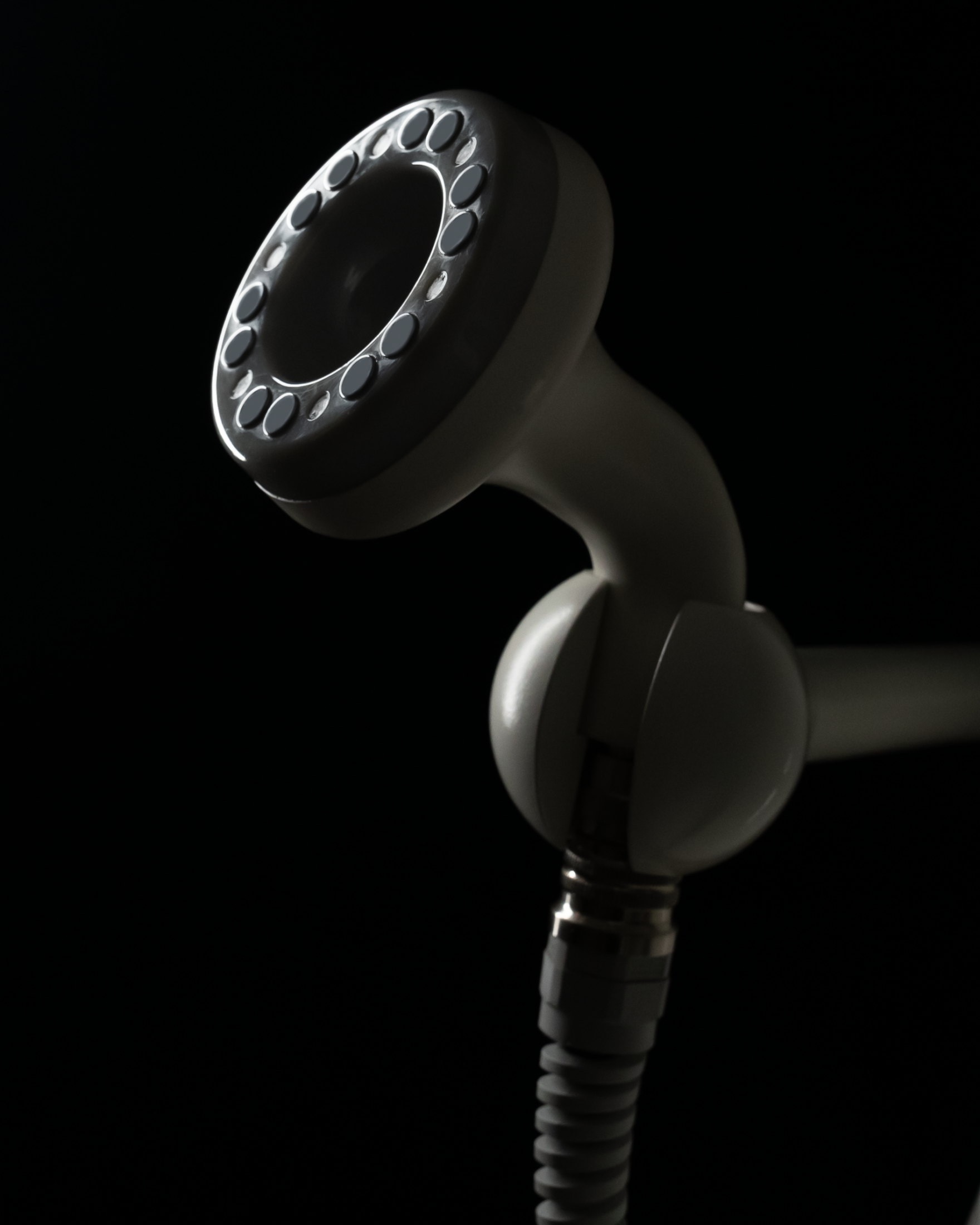 White shower head with dark background, backlit, showing nozzle and hose.
