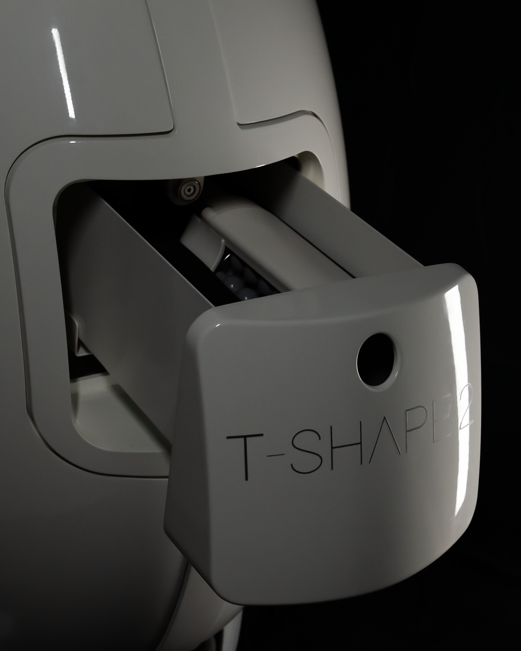 A close-up of a white device with a T-shaped part partially extended. The device is in a dark setting.