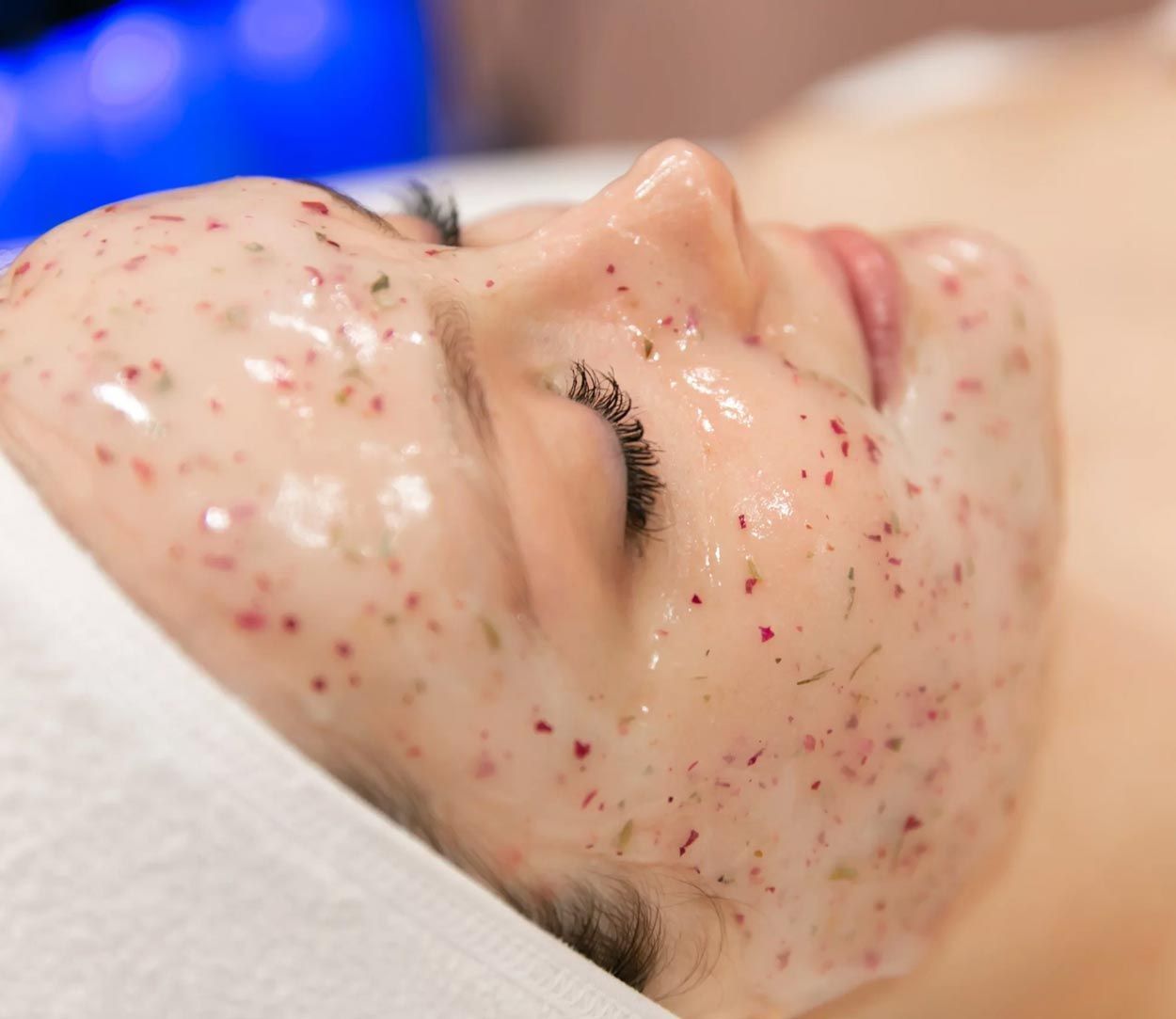 Woman with a facial mask, lying down. Mask is clear with red and green specks.
