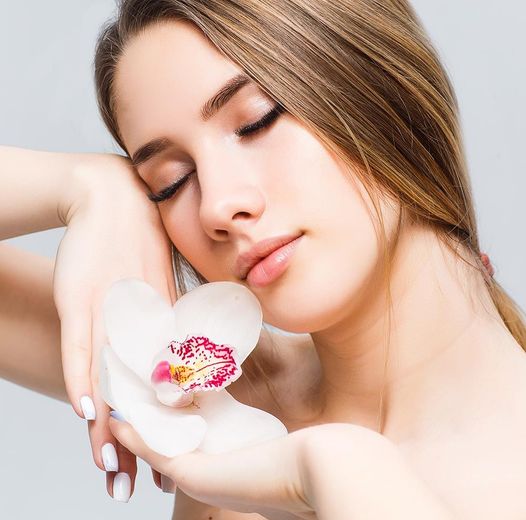Woman with eyes closed, holding a white orchid, skin tone light.