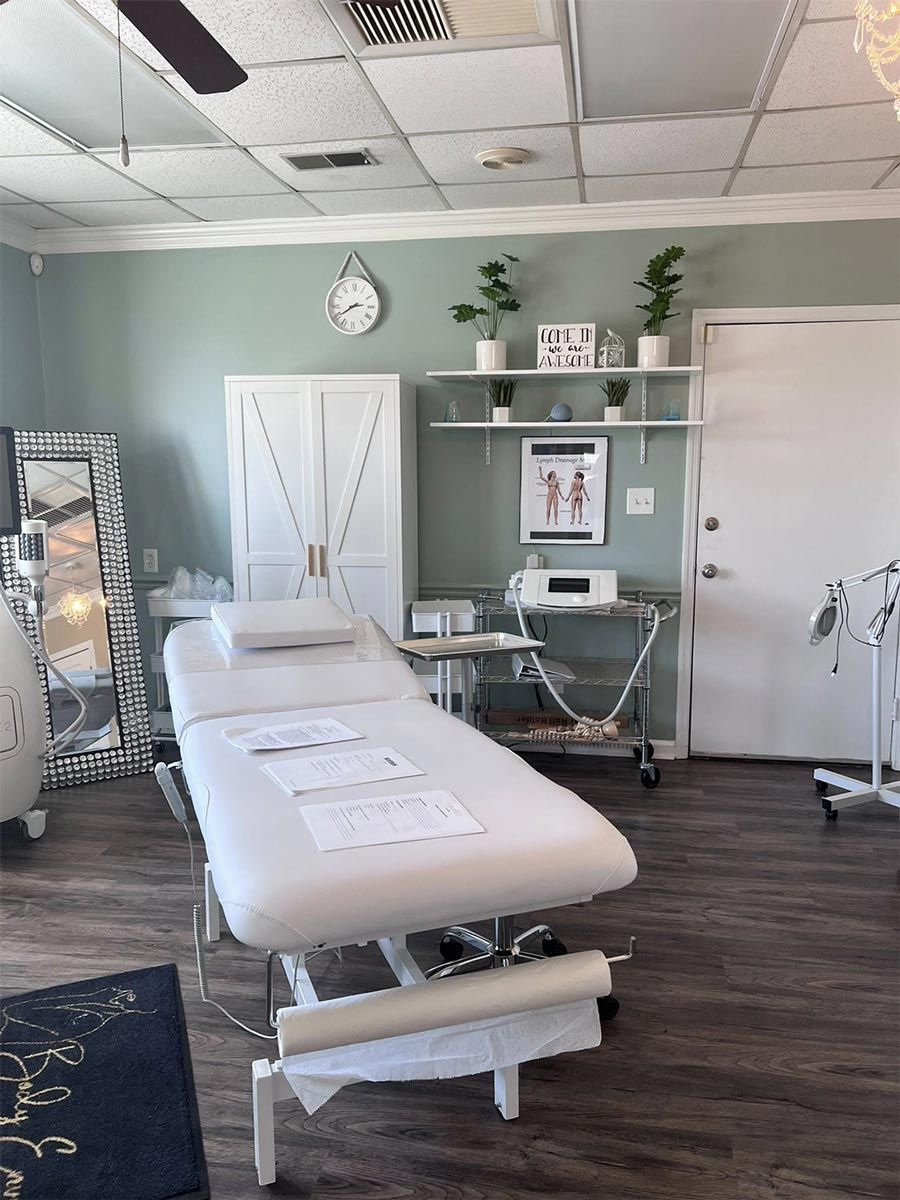 Treatment room with massage table, white cabinets, and plants on shelves, sage green walls.