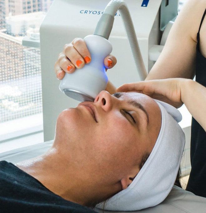 Woman receiving a cryotherapy facial treatment; a technician uses a handheld device on her face.