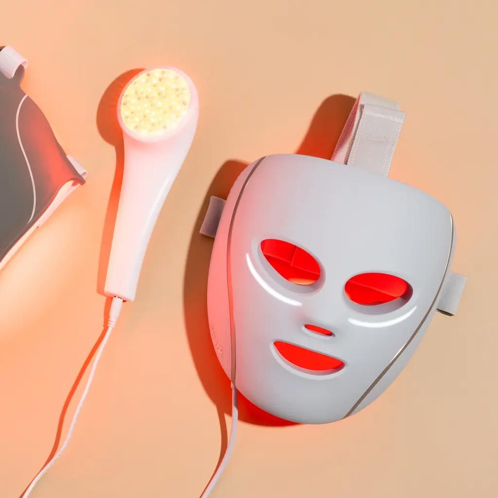 LED light therapy mask and wand, emitting red light, against a light orange background.
